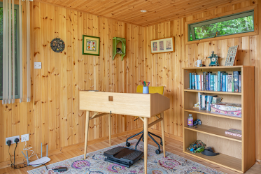 Interior Home Office Design Timber-lined garden office interior with a wooden desk, chair, bookshelf and framed artwork.
